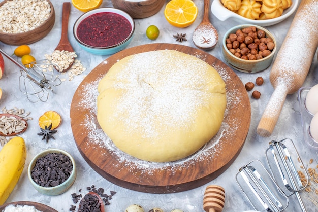 Vooraanzicht van rauw gebakmeel op ronde rasp, vers fruit, jamkoekjes op een gebeitste witte achtergrond