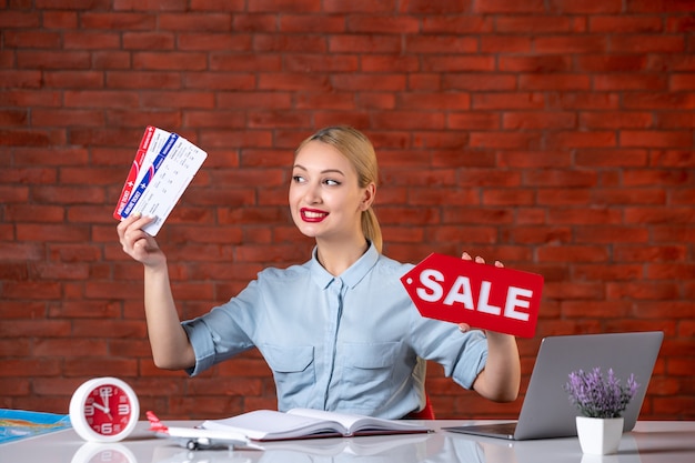 Foto vooraanzicht van reisagent zittend achter haar werkplek met kaartjes en verkoop naambordje global managers binnenshuis bureau bezetting assistent toerisme kaart