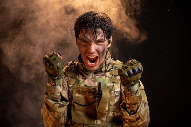 Vooraanzicht van schreeuwende jonge soldaat in uniforme donkere muur