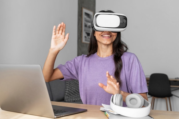 Foto vooraanzicht van smileyvrouw met behulp van virtual reality headset thuis met laptop