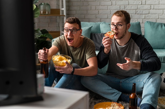 Foto vooraanzicht van twee mannelijke vrienden die bier met pizza hebben en naar sport op tv kijken