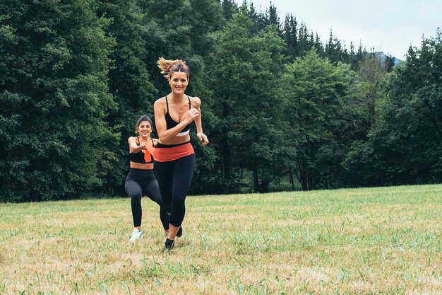 Vooraanzicht van twee vrouwen die krachtoefeningen doen met een rubberen band, veel moeite doen midden in het bos