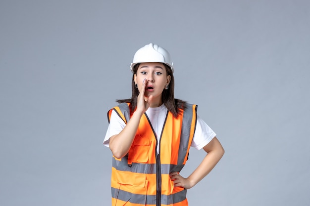 Vooraanzicht van vrouwelijke bouwer in uniforme en beschermende helm op grijze muur