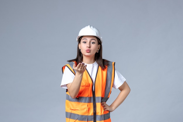 Vooraanzicht van vrouwelijke bouwer in uniforme en beschermende helm op grijze muur