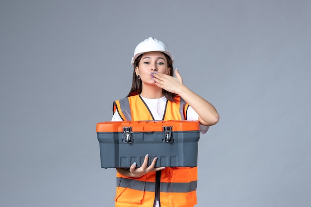 Vooraanzicht van vrouwelijke bouwer met gereedschapskoffer op grijze muur
