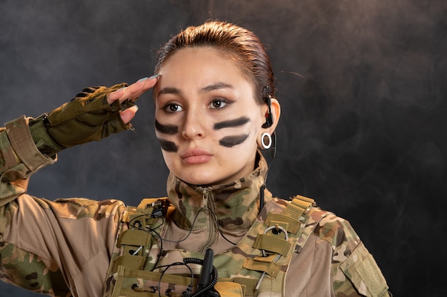 Vooraanzicht van vrouwelijke soldaat in camouflage die op de donkere muur salueert