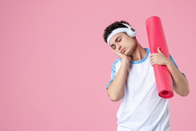 Vooraanzicht vermoeide jonge man in sportkleren met yogamat