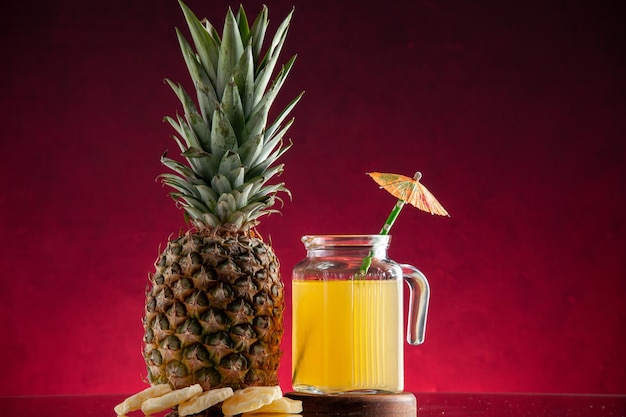 vooraanzicht vers ananassap in glazen karaf op houten bord ananas fruit droge ananasringen op rode achtergrond vrije ruimte
