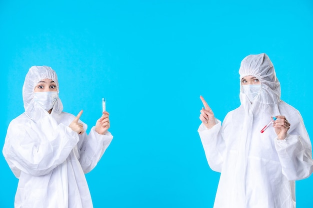 vooraanzicht vrouwelijke artsen in beschermende pakken en maskers die kolven op de blauwe achtergrond houden medisch ziekenhuis gezondheidswetenschap covid-pandemie virus