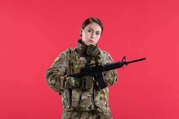 Vooraanzicht vrouwelijke soldaat in camouflage met machinegeweer rode muur