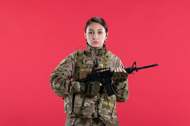 Vooraanzicht vrouwelijke soldaat in militair uniform met machinegeweer rode muur