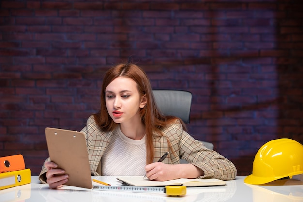 vooraanzicht vrouwelijke werknemer binnen bouwplaats zittend achter tafel met documenten ingenieur aannemer manager bedrijfsplan job