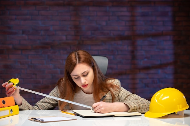 vooraanzicht vrouwelijke werknemer in bouwplaats zittend achter tafel met meetlint baan agenda bedrijfsplan bedrijfsingenieur manager