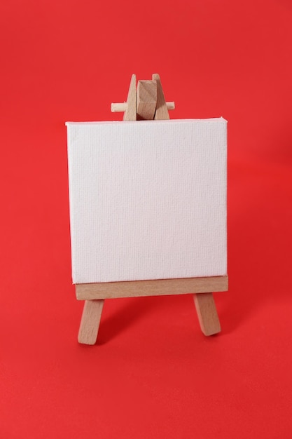 Vooraanzicht wit mini canvas met houten ezel op rode achtergrond