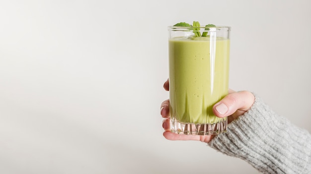 Foto vooraanzichthand die groene smoothie en munt in glas met exemplaar-ruimte houden