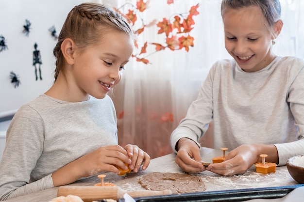 Voorbereiden om Halloween te vieren en een traktatie voorbereiden. Mooie meisjes kijken naar uitgesneden halloween-koekjes van deeg en glimlachen in de thuiskeuken. levensstijl