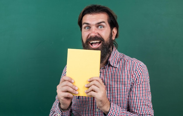 Foto voorbereiden op examen met boek college docent op les terug naar school formeel onderwijs kennis dag volwassen bebaarde leraar bij les brutale man werk in de klas met schoolbord