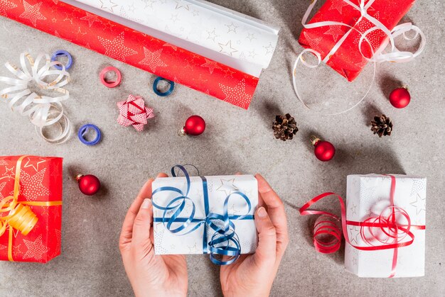 Foto voorbereiding op kerstvakantie. geschenken en decoraties op de tafel, meisje handen in de afbeelding houdt een van geschenken. bovenaanzicht