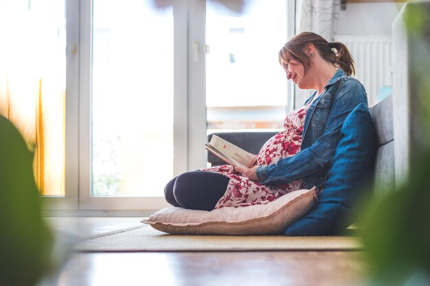 Voorbereiding op zwangerschap Zwangere blanke moeder zit op de grond een boek te lezen over baby's