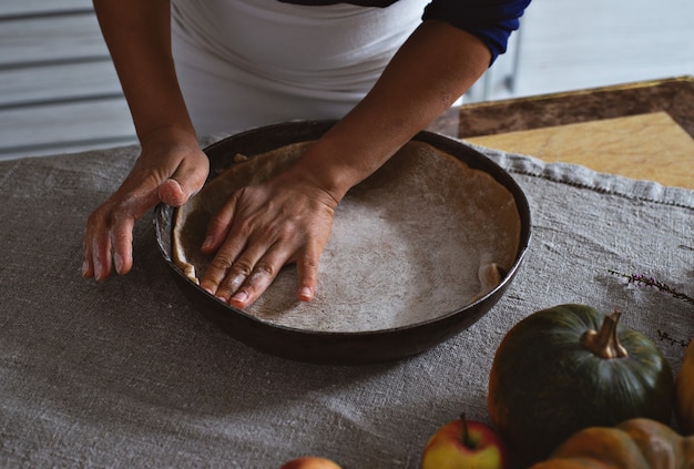 Voorbereiding, Thanksgiving Day-viering. Een kok doet het deeg in een ijzeren vorm. Maakt het deeg glad met haar handen. Vlakbij op de tafel staan appels en pompoenen.