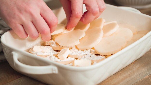 Voorbereiding van geschulpte aardappelen in een witte keramische ovenschaal.