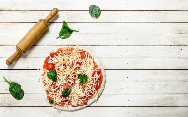 Voorbereiding van pizza met verschillende ingrediënten. Op een witte houten tafel.