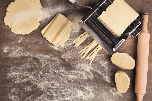 Voorbereiding van zelfgemaakte fettuccine op pastamachine. Bovenaanzicht op rauw deeg en speciale apparatuur voor het maken van traditionele Italiaanse maaltijden, kopieer ruimte