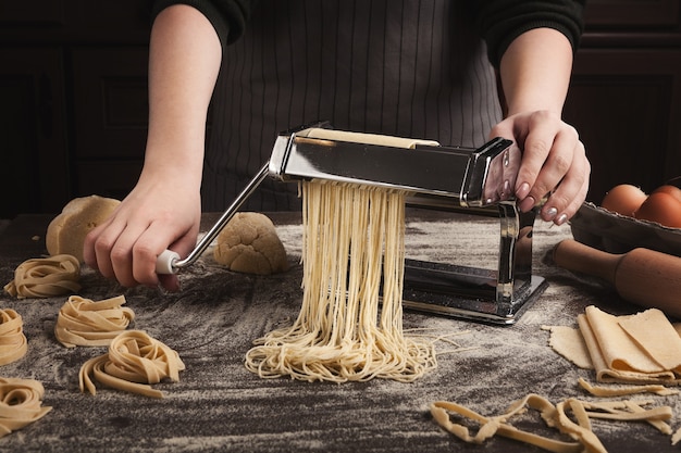 Voorbereiding van zelfgemaakte fettuccine op pastamachine. Rauw deeg snijden tot tagliatelle op speciale apparatuur, traditioneel Italiaans keukenconcept, kopieerruimte