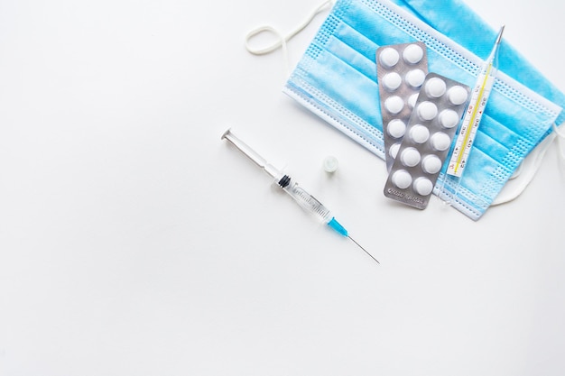 Voorbereiding voor vaccinatie tegen covid-19. Spuit, vaccin, pillen, medisch masker op een witte tafel. Uitzicht van boven.