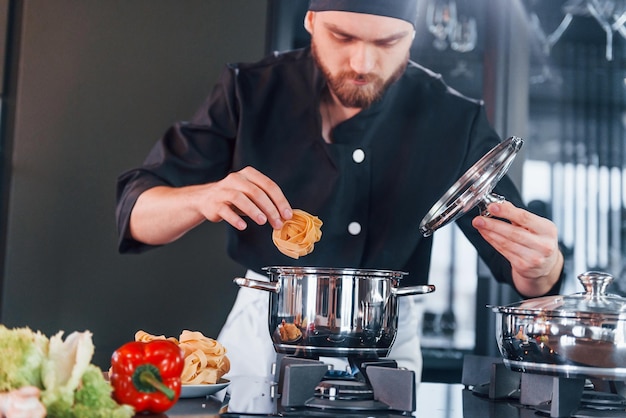 Voorbereidingsproces Professionele jonge chef-kok in uniform die aan de keuken werkt