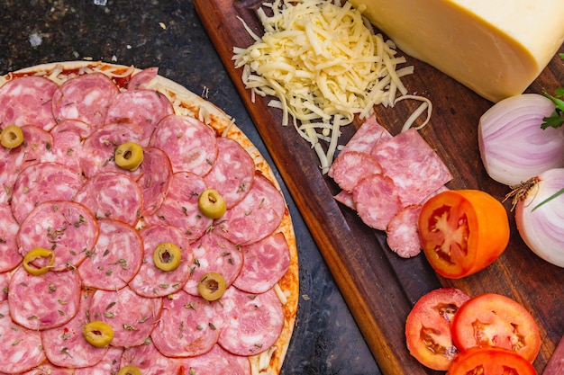 Voorgebakken pepperoni-pizza met verse pizza-ingrediënten op een houten bord