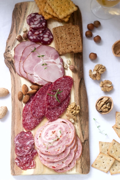 Voorgerecht van verschillende soorten worst, vlees, kaas en crackers op een houten bord, geserveerd aan wijn.