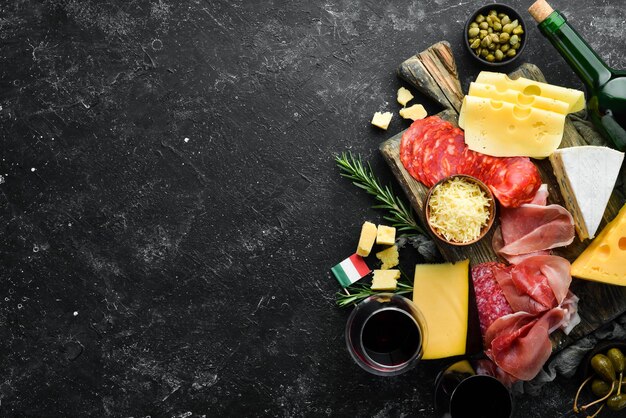 Voorgerechten tafel met Italiaanse antipasti snacks en wijn in glazen Kaas wijn salami en prosciutto op een zwarte stenen achtergrond Bovenaanzicht vrije ruimte voor uw tekst