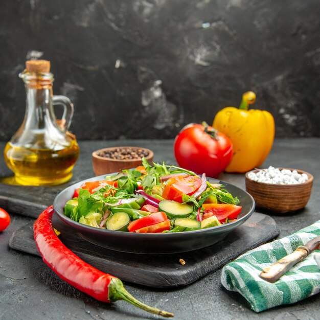 voorkant van een veganistische salade met verse ingrediënten op een bord en peper op een zwarte snijplank