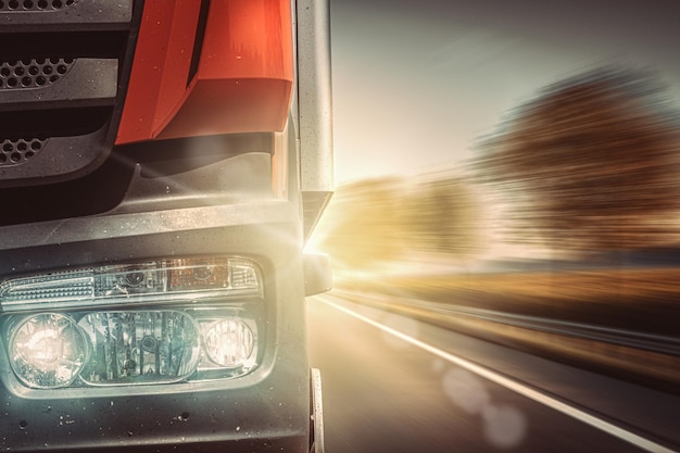 Foto voorkant van snel bewegende vrachtwagen met lichten aan op landweg met zonnestralen