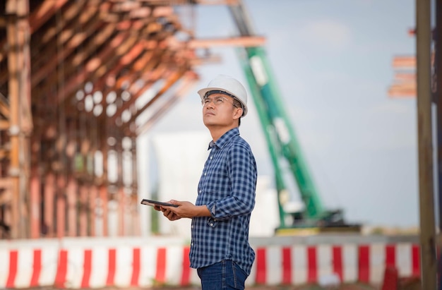 Voorman werknemer in veiligheidshelm op de bouwplaats van de infrastructuur Bouwingenieur die project op de bouwplaats controleert Architect met een digitale tablet op een bouwplaats