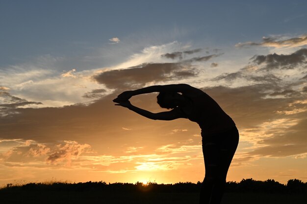 Voorschot van slanke jonge vrouw die yoga palm pose doet in het gouden uur