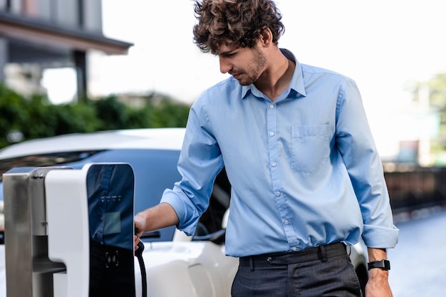 Vooruitstrevende zakenman steekt de stekker van de oplader van het laadstation in de EV