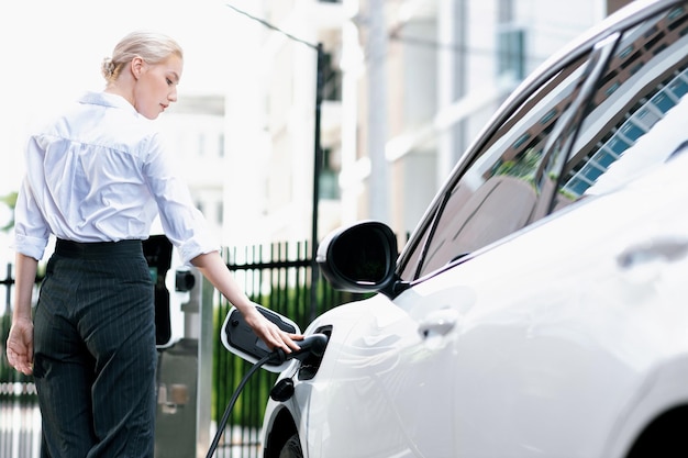 Vooruitstrevende zakenvrouw steekt de stekker van de oplader van het laadstation in de EV