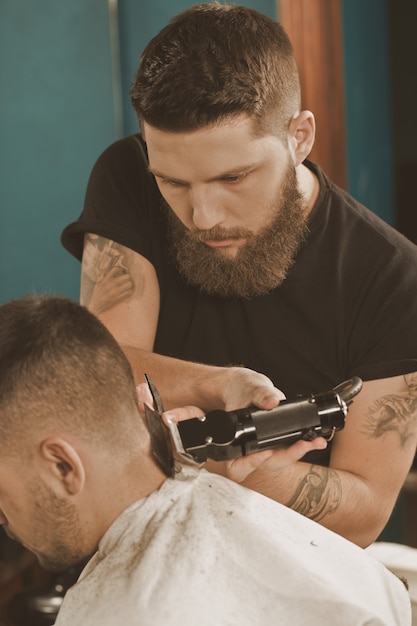 Voorzichtig werk. Verticaal portret van een kapper die aan het kapsel werkt met een trimmer