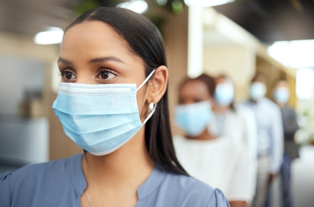 Voorzichtigheid betrachten Bijgesneden opname van een aantrekkelijke jonge zakenvrouw die een masker draagt terwijl ze vooraan in de rij staat in haar kantoor