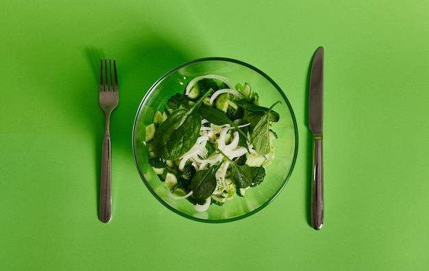 Vork en mes in de buurt van een bord met groene salade. Plat leggen.