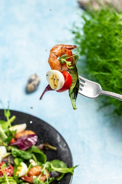 Vork met salade van groenten cherry tomaten, komkommer, avocado, eieren en gerookte garnalen. spatten van citroensap, schoon eten. voedsel recept achtergrond. detailopname.