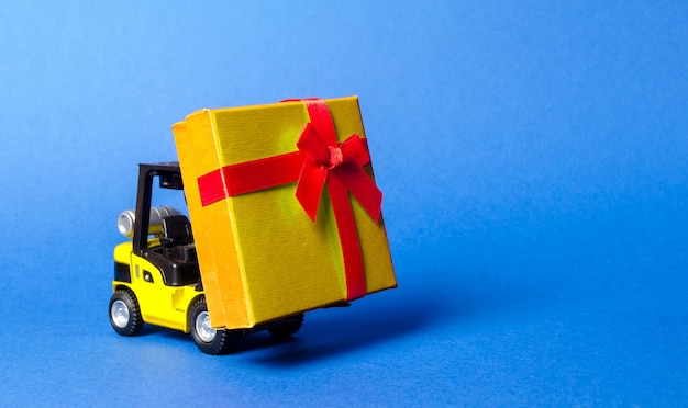 Vorkheftruck draagt een goudgele geschenkdoos met een rode strik Aankoop en levering van een cadeau