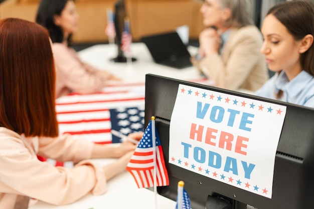 Photo voter sitting at registration table registering at polling station decorated with american flag