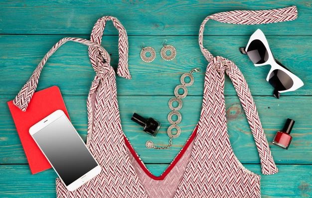 Insieme di concetto di viaggio di roba da donna con l'accessorio del blocco note dello smart phone del vestito sulla scrivania di legno blu