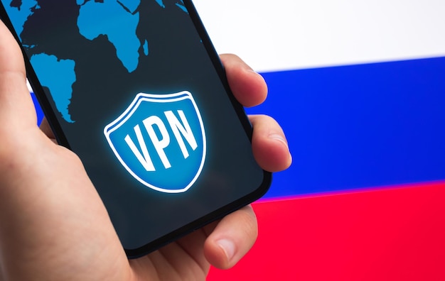 VPN в России Безопасный и конфиденциальный интернет Заблокированные сайты Рука с мобильным телефоном и приложением VPN Флаг и ноутбук на заднем плане фото