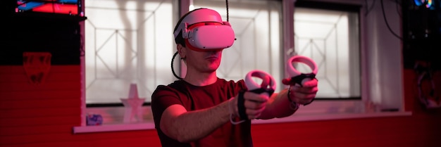 Фото Виртуальная игра и человек-геймер виртуальной реальности весело играют в футуристический симулятор видеосъемки в 3d-очках и джойстиках в развлекательной виртуальной комнате с инновационными технологиями и баннером с неоновым светом