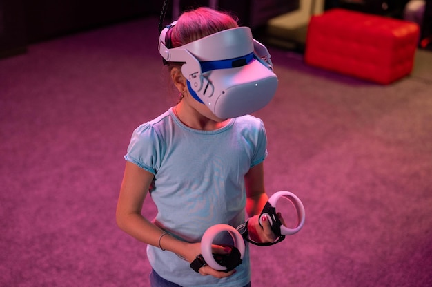 VR game en virtual reality kid girl gamer acht jaar oud leuk spelen op futuristische simulatievideogame in 3D-bril en joysticks in entertainment vr room innovation technology en neonlicht