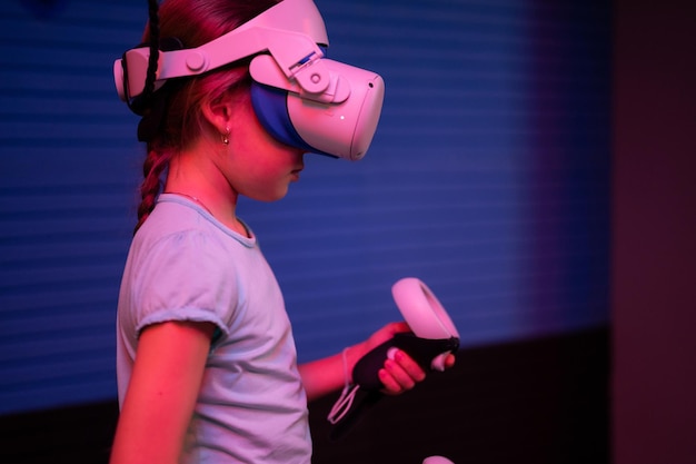 VR game en virtual reality kid girl gamer acht jaar oud leuk spelen op futuristische simulatievideogame in 3D-bril en joysticks in entertainment vr room innovation technology en neonlicht